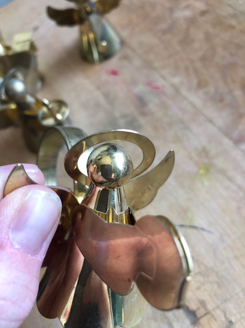 May include: Gold metal angel napkin ring with a halo and wings. The angel is holding a napkin.