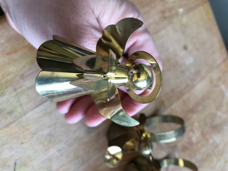 May include: A set of gold metal angel napkin rings. The angels have a bell-shaped skirt, wings, and a halo.