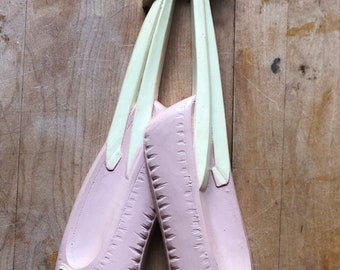 May include: A pair of pink ballet slippers with cream-colored ribbons and bows. The decorative wall hanging features detailed stitching and a bow at the top for hanging. The slippers are a soft pink color.