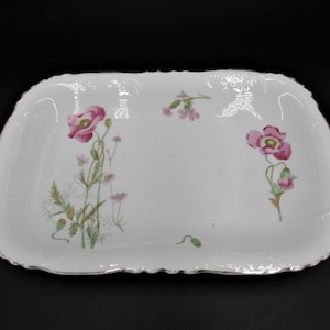 May include: A white rectangular serving platter with a gold rim and a floral design featuring pink poppies and green leaves.