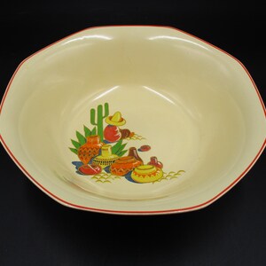 May include: A large, octagonal, cream-colored ceramic bowl with a red rim. The bowl features a colorful design of cacti, pottery, and a sombrero.