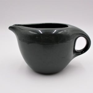 May include: A dark grey ceramic gravy boat with a handle. The boat has a smooth, glossy finish.