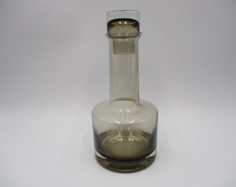 May include: A clear glass bottle with a brown glass stopper. The bottle has a rounded bottom and a cylindrical neck.