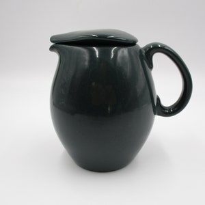 May include: A dark green ceramic pitcher with a lid and a handle. The pitcher has a rounded body and a smooth finish.