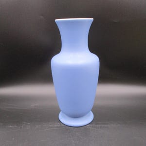 May include: A light blue ceramic vase with a rounded body and a flared lip. The vase has a smooth, matte finish.