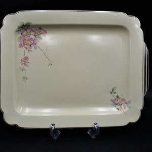 May include: A white ceramic serving tray with a gold rim and floral design. The tray has two handles on the sides and features pink and green flowers.