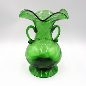 May include: A green glass vase with a ruffled top and two handles. The vase has a swirl design and a round base.