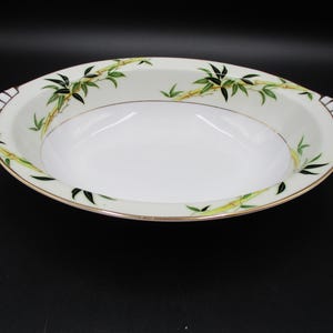May include: Oval serving dish with a white interior and a gold rim. The dish features a bamboo design with green leaves and yellow stalks. The handles have a black and white striped design.