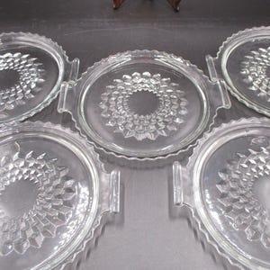 May include: Set of four clear glass serving plates with a raised, textured design. Each plate has two handles on the sides.