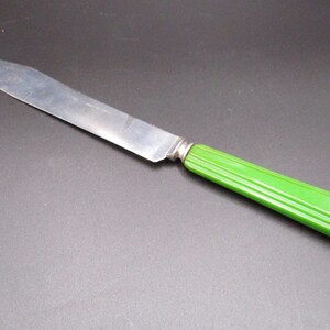 May include: A vintage silver butter knife with a green plastic handle. The handle has a ridged design.