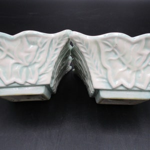 May include: Two square ceramic planters with a light green glaze and white leaf design. The planters have a square base.