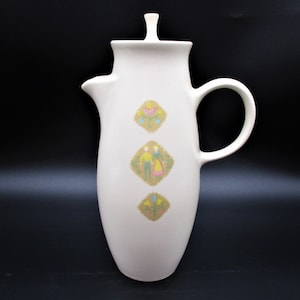 May include: White ceramic coffee pot with a lid and a handle. The pot has a stylized folk art design with yellow, pink, and green accents.