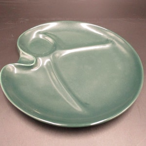 May include: A green ceramic divided serving plate with three sections. The plate has a rounded shape and a smooth, glossy finish.