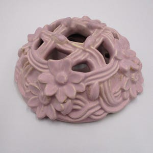 May include: A pale pink ceramic planter with a floral design. The planter has a lattice-like pattern and is shaped like a dome.