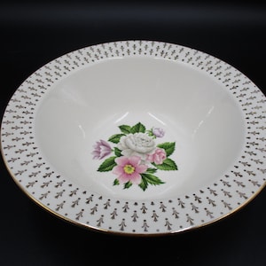 May include: White ceramic bowl with a gold rim and a floral design featuring pink and white roses. The bowl has a black and gold pattern around the rim.