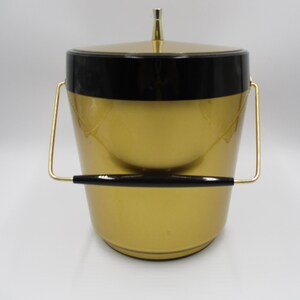 May include: Gold ice bucket with a black lid and a gold handle. The bucket has a shiny finish.