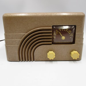 May include: A vintage brown radio with a curved speaker design and yellow knobs. The radio features a dark brown dial with a yellow needle and numbers. The radio's design is reminiscent of mid-century electronics.