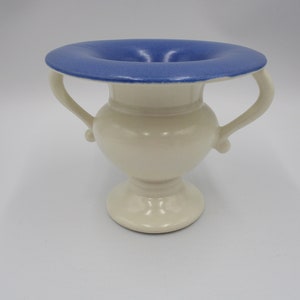 May include: A white ceramic vase with two handles and a blue glazed top. The vase has a classic urn shape.
