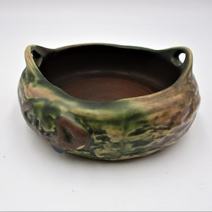 May include: A green and brown ceramic bowl with two handles. The bowl has a textured surface and a floral design.