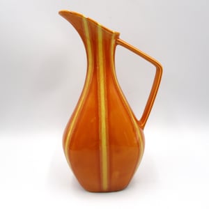 May include: Orange ceramic jug with a curved spout and a handle. The jug has vertical yellow stripes. The jug is a decorative item.