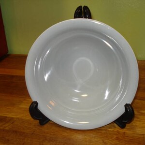 May include: A white ceramic bowl with a slightly rippled edge. The bowl is sitting on a wooden stand.