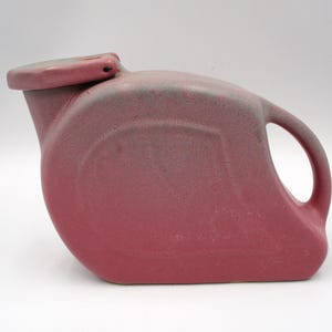 May include: A maroon ceramic pitcher with a handle and a lid. The pitcher has a rounded body and a spout. The handle is a simple loop. The lid is attached with a hinge. The pitcher has a speckled texture.