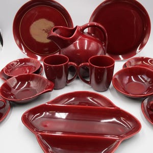 May include: A set of burgundy red ceramic dinnerware, including plates, bowls, mugs, and a pitcher. The set features a simple, elegant design.