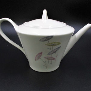 May include: White ceramic teapot with a floral design featuring pink, blue, green, and yellow flowers. The teapot has a lid and a handle.