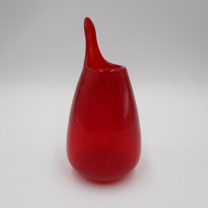 May include: A vibrant red glass vase with a unique, elongated spout. The vase has a teardrop shape and a smooth, glossy finish. This decorative piece is ideal for displaying flowers or as a standalone art object.