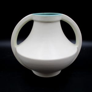 May include: White ceramic vase with two large, rounded handles. The vase has a light blue rim and a slightly flared base.