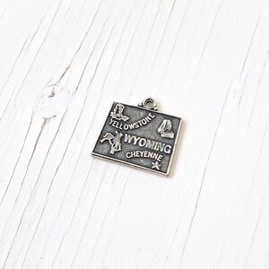 May include: Silver charm depicting a map of Wyoming with the text "Yellowstone", "Wyoming", and "Cheyenne". The charm also includes images of a cowboy riding a horse, a boot, and a mountain.