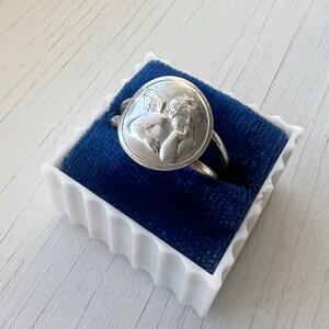 May include: A silver ring with a cherub design in a blue velvet ring box.