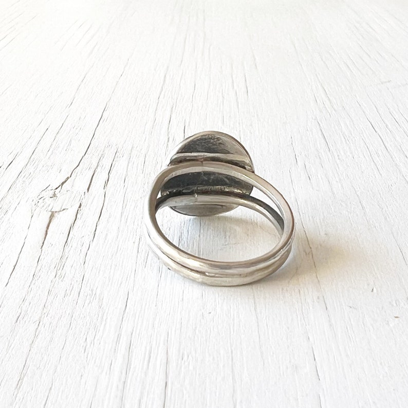 May include: A silver ring with a round, textured top. The ring is made of two bands that are joined together.