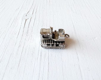 May include: A silver charm in the shape of a bulldozer. The charm has a detailed design and is perfect for adding to a bracelet or necklace.