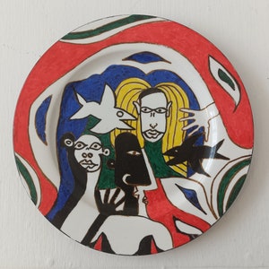 Może przedstawiać: Biały ceramiczny talerz z kolorowym abstrakcyjnym wzorem. Wzór zawiera czerwony, zielony, niebieski i żółty schemat kolorów. Talerz ma czarną obwódkę i białe tło. Wzór zawiera stylizowane figury i rybę.