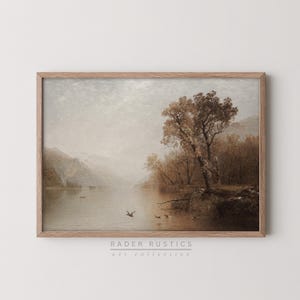 Pode incluir: Uma impress&atilde;o emoldurada de uma paisagem com uma serena cena lacustre com &aacute;rvores e montanhas em tons suaves. A obra de arte tem uma est&eacute;tica vintage, com uma moldura de madeira castanha clara. A impress&atilde;o inclui o texto "RADER RUSTICS art collective".