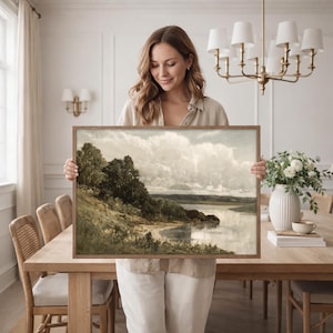 May include: A framed landscape painting featuring a serene waterscape with a cloudy sky. The artwork depicts a shoreline with trees and a body of water, framed in a wooden border. The painting evokes a sense of tranquility and natural beauty.