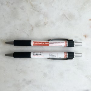 Pode incluir: Duas canetas pretas e prateadas com etiquetas brancas. A caneta superior diz "Succinylcholine" e a caneta inferior diz "200 mg por 10 mL (20 mg por mL)".