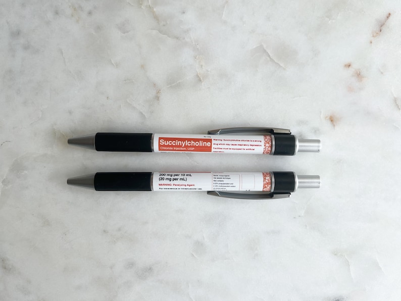 Pode incluir: Duas canetas pretas e prateadas com etiquetas brancas. A caneta superior diz "Succinylcholine" e a caneta inferior diz "200 mg por 10 mL (20 mg por mL)".