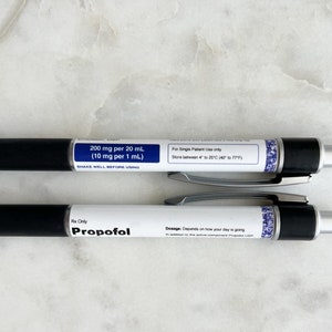 Pode incluir: Duas canetas pretas e prateadas com etiquetas brancas. A caneta superior tem o texto "200 mg por 20 mL (10 mg por 1 mL)" e "Para uso exclusivo de um &uacute;nico paciente. Armazenar entre 4&deg; e 25&deg;C (39&deg;F e 77&deg;F)". A caneta inferior tem o texto "Rx Only Propofol" e "Dosagem: Depende de como est&aacute; sendo o seu dia".