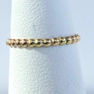 May include: A delicate gold ring made of small beads. The ring is two-toned, with half of the beads being a rose gold colour and the other half being a yellow gold colour.