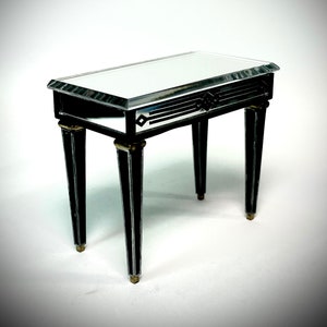 Puede incluir: Una pequeña mesa auxiliar de espejo negro con detalles dorados y cuatro patas. La tapa de la mesa tiene un diseño geométrico.