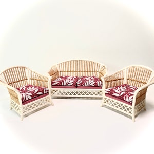 Op de afbeelding: Een witte rieten bank en twee bijpassende stoelen met rode en witte bloemenkussens. De meubels zijn in een rij op een witte achtergrond gerangschikt.