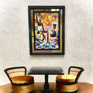 May include: Two miniature chairs with brown wicker backs and gold velvet seats sit on a wooden surface in front of a black table with a checkered top. A framed painting of two women playing chess hangs on the wall behind the table.