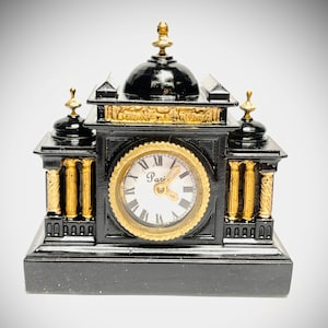 May include: A black and gold decorative clock with a domed top and Roman numeral clock face. The clock has gold accents and a rectangular base. The clock face reads "Paris".