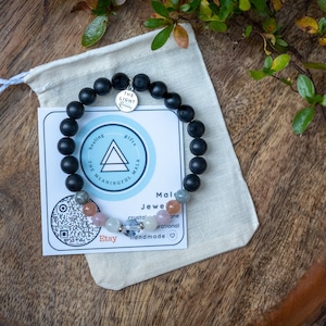 May include: Black beaded bracelet with a silver charm that says "The Light Within". The bracelet is on a white fabric pouch with a card that says "Healing Gifts The Meaningful Mala" and "Mald Jewe crystal one rational handmade:❤♡❤♡".