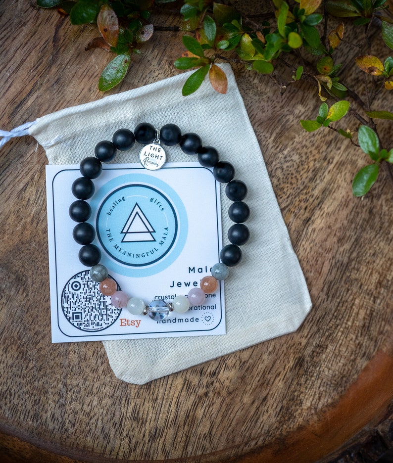 May include: Black beaded bracelet with a silver charm that says "The Light Within". The bracelet is on a white fabric pouch with a card that says "Healing Gifts The Meaningful Mala" and "Mald Jewe crystal one rational handmade:❤♡❤♡".