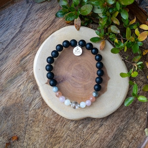 May include: A black beaded bracelet with a silver charm that says "Mom" and a mix of light pink, gray, and white beads.
