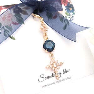 May include: A gold-toned charm featuring a dark blue square crystal and a star-shaped crystal pendant, attached to a navy blue sheer ribbon. The display card includes the text "Something blue" and "Handmade by Bellsnbliss" in black script.