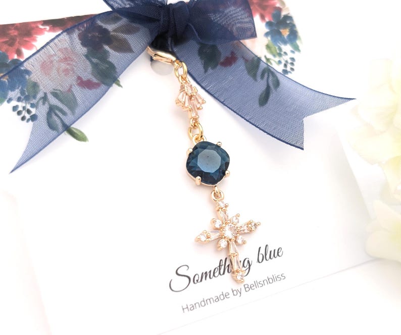 May include: A gold-toned charm featuring a dark blue square crystal and a star-shaped crystal pendant, attached to a navy blue sheer ribbon. The display card includes the text "Something blue" and "Handmade by Bellsnbliss" in black script.